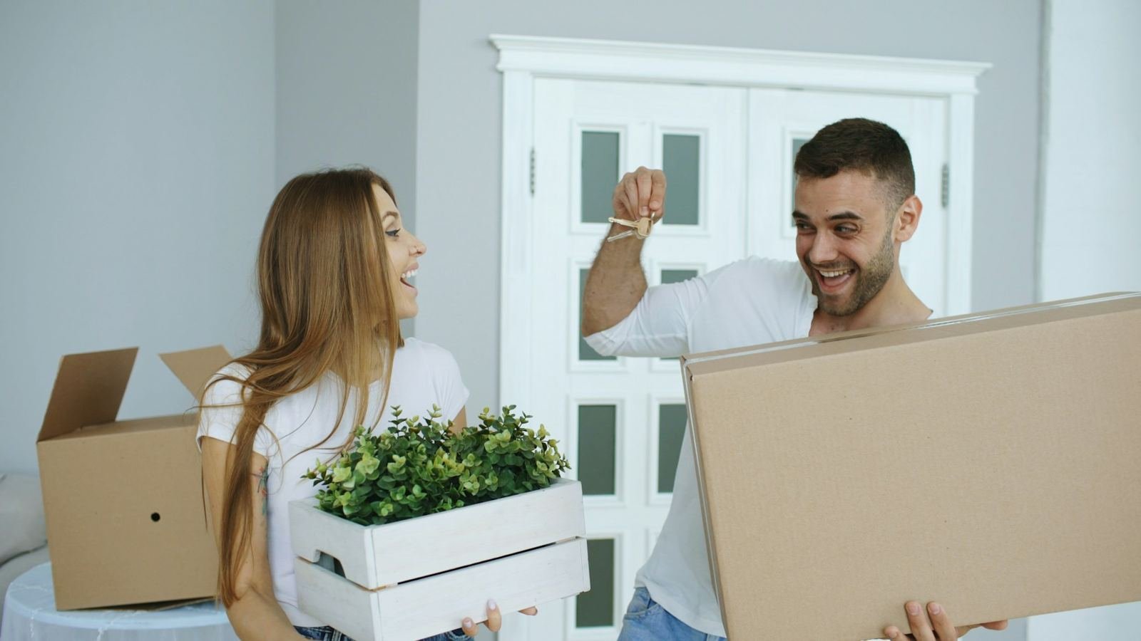 A young couple carrying moving boxes and holding up the keys to their first home