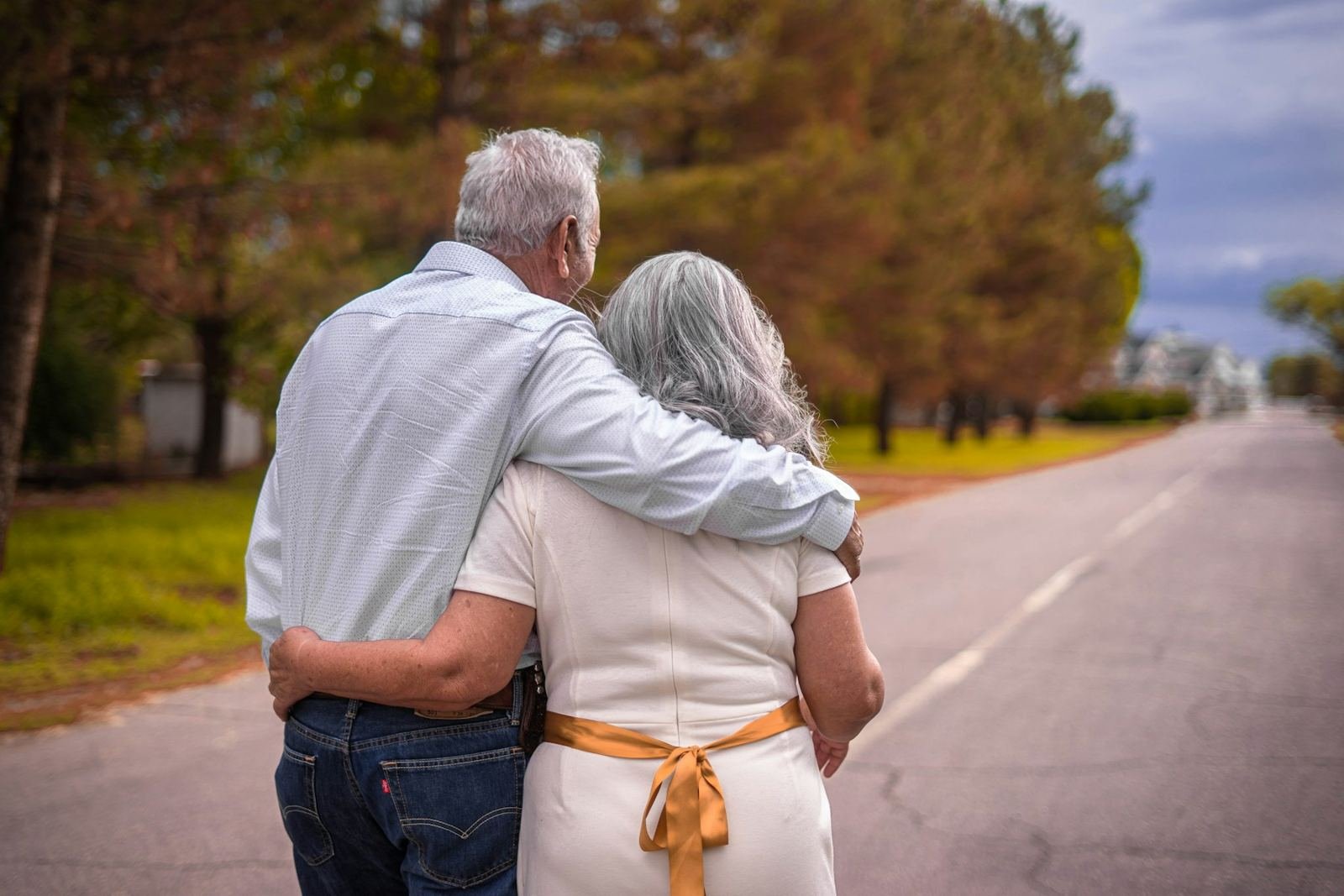 An older couple walking arm in arm along a tree lined road